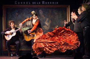 Una mujer con un vestido rojo bailando flamenco rodeada de músicos