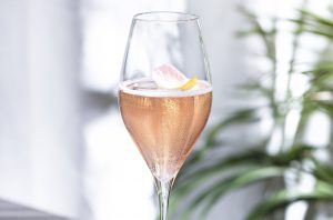 Cóctel rosa espumoso en una copa de champán con plantas al fondo
