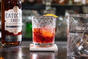 Cóctel rojo en un vaso bajo en la parte superior de un bar con una botella de whisky