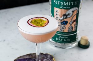 Un martini rosado con una rodaja de maracuyá frente a una botella de ginebra